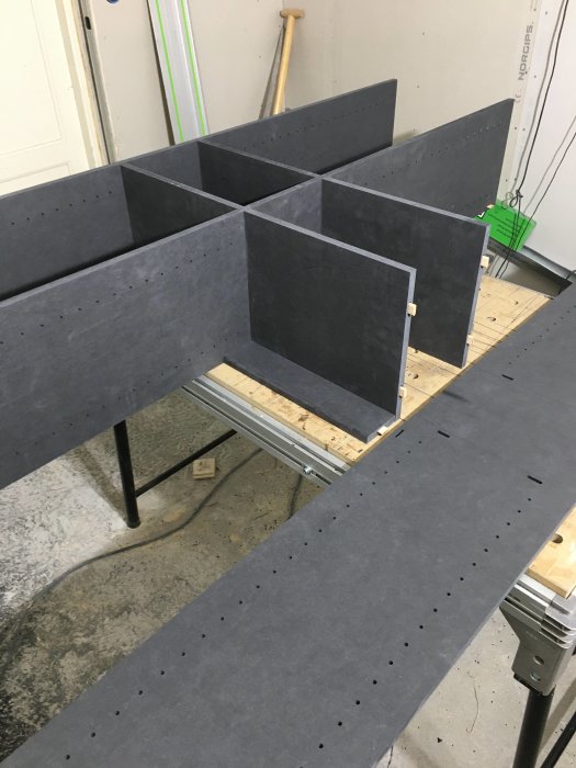 Utsågade delar i mörkt material för högskåpsmöbel med markerade hål för montering.