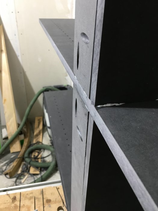 Hörn av svartmålade träpaneler med felplacerad trädomino och limrester som ska slipas.