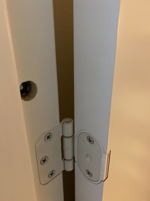 Vit dörr med öppet justerbart gångjärn mellan dörr och karm.