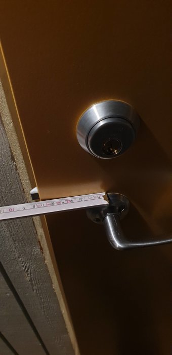 Närbild på en Assa Abloy dörrlås och handtag med måttband för dimensionering.