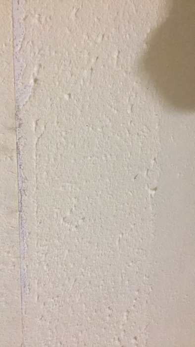 Vägg med ojämn yta och rester av tapetludd efter borttagen tapet.