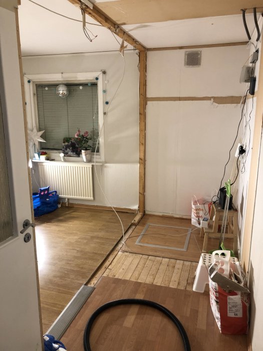 Rum under renovering där en vägg är delvis riven inför installation av garderober, med synligt fönster.