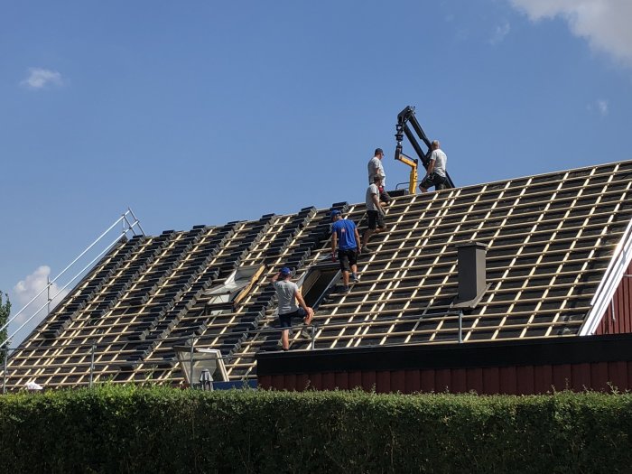 Arbetare som byter tak på ett en och halvplans hus från 1969, gamla takfönster syns.