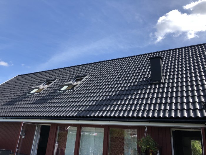 Hus med nytt tak och takfönster mot en blå himmel, inklusive en solcellsdriven Velux-fönster.