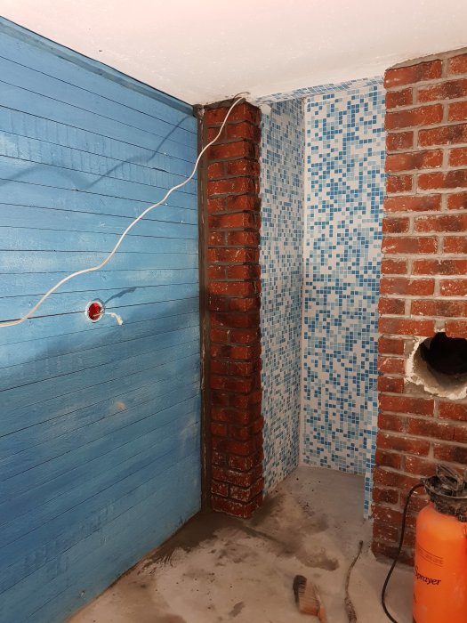 Hörn av ett rum under renovering med nyligen fogade dekorstenar på en vägg och blåmålade träväggar.