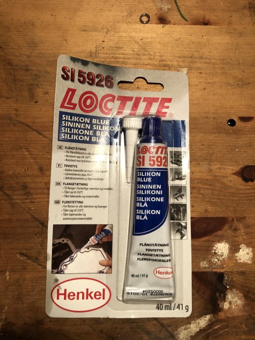 Förpackning av Loctite SI 5926 blått silikon i ett försäljningspaket på ett träbord, är möjligt tätmedel för fönsterbleck.