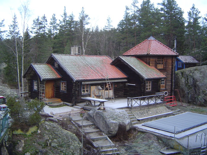 Timrad byggnad med ytterdörrar, omgivet av natur, potentiell plats för planerad svale.