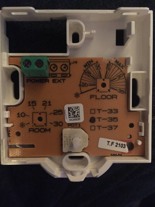 Elektronisk termostat öppnad för att visa kretskort och komponenter med inställningsrattar och anslutningspunkter.