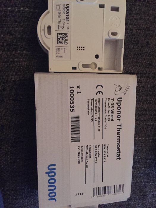 Uponor T35 termostat och dess förpackning visas på en matta, ingen teknisk analys synlig.