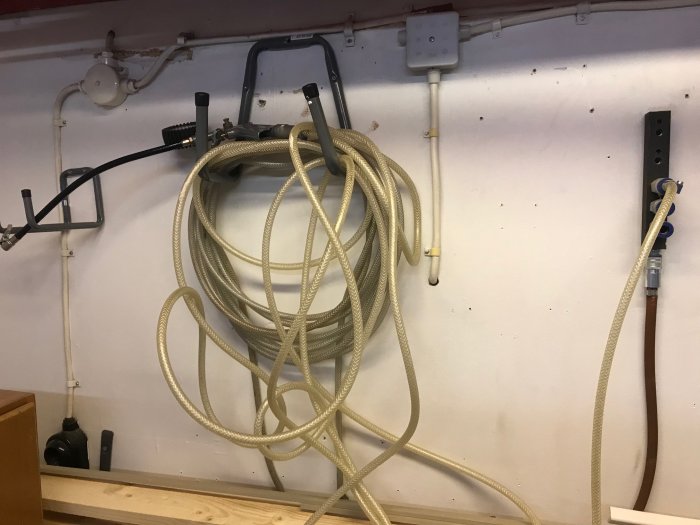 Gammal kompressor med 5 meters slang upphängd på en verkstadsvägg med eluttag och rör i bakgrunden.