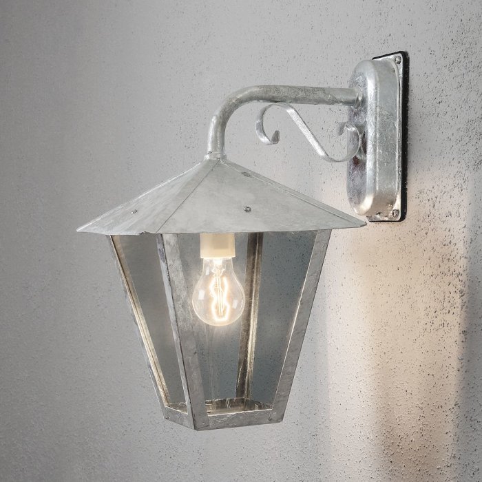 Grå väggmonterad lykta i äldre stil med synlig glödlampa, monterad på en strukturerad vägg.