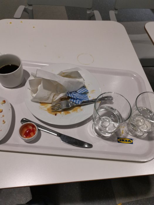 Ett matbord med rester av köttbullar, såsfläckar, två tomma glas, en kaffekopp och en IKEA-brikett.