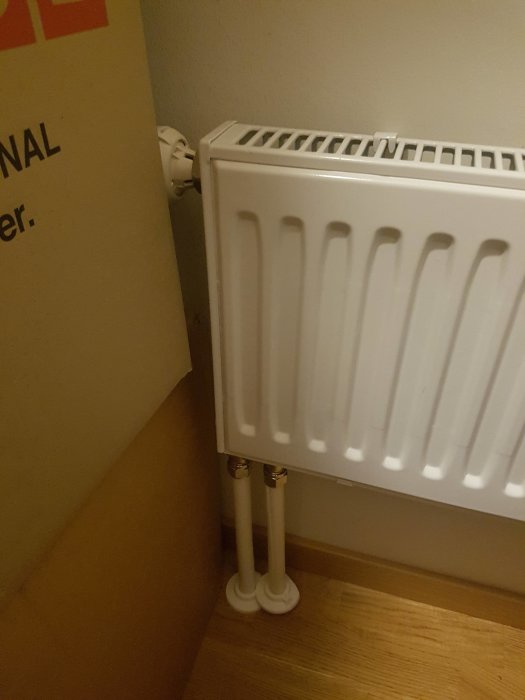 En kall radiator med termostat och anslutna rör i ett hörn av ett rum.