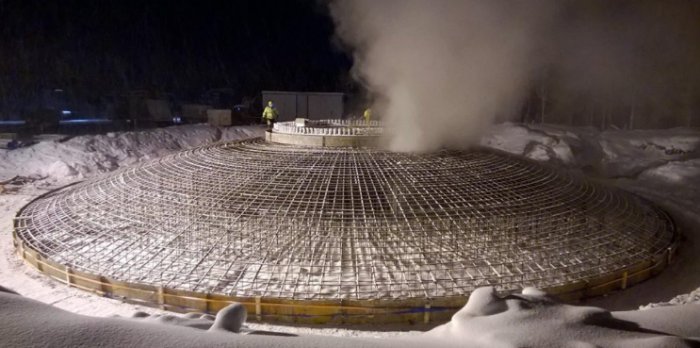 Stort betongfundament för vindkraftverk under nattetid täckt av snö med arbetare och ånga i bakgrunden.