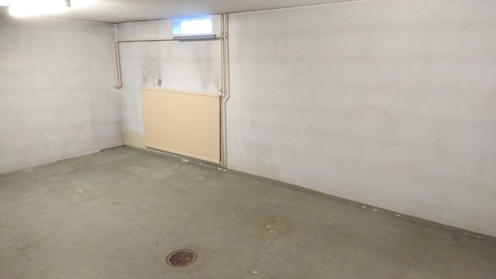 Bild på ett tomt tidigare källargarage med slitet grönt golv, sprickor och en golvbrunn, redo för renovering.