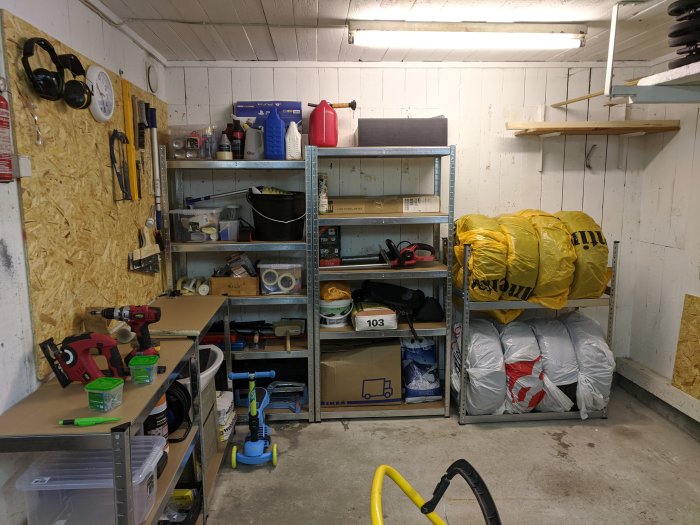 Organiserat garage med hyllor, verktygsbräda och utrustning, och några IKEA säckar.