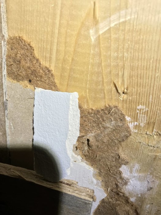 Gipsbit med skimrande skikt framträdande mot en grov vägg i rivet kök.