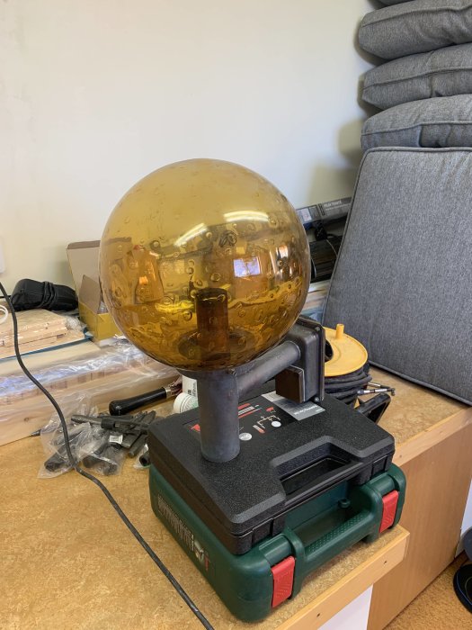 Kopparlampa med hel glasglob på verktygslåda, inomhusmiljö.