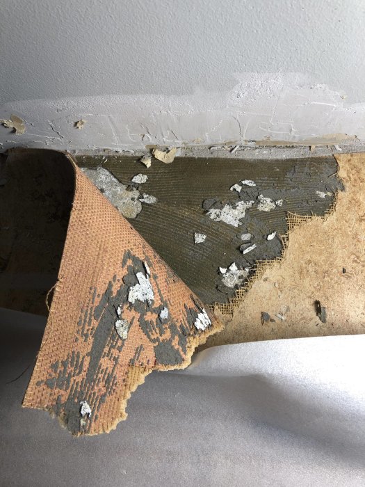 Golvrenovering där en gammal limmad matta är delvis borttagen och visar underliggande avjämningsmassa.
