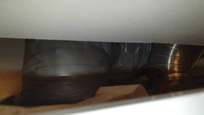 En panna dold bakom en lucka i ett badrum, synbar genom en smal öppning med begränsad sikt.