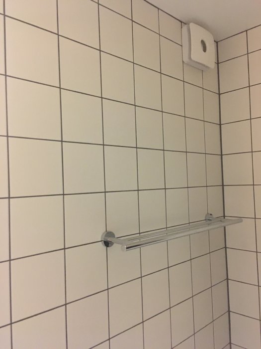 Badrumsvägg med kakel, handdukshängare och fläkt installerade, redo för fogning.