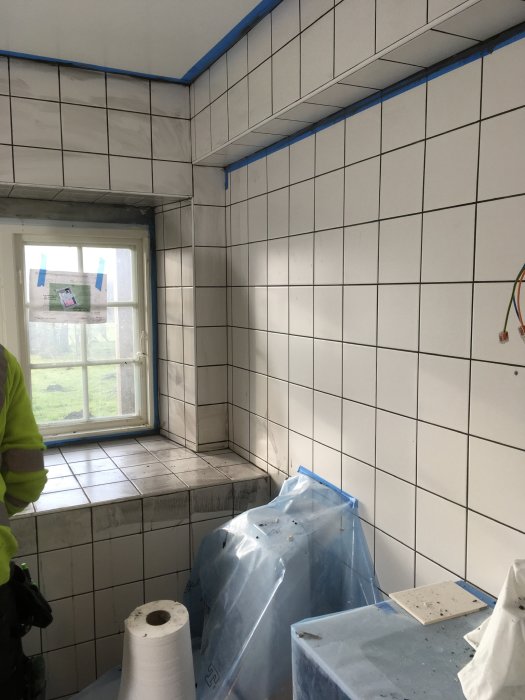 Badrum under renovering med vita kakelväggar, blå tejp markerar för fogning.