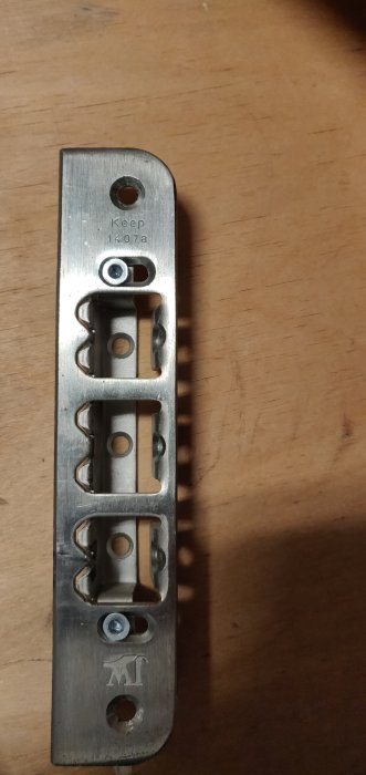 Ett metalliskt slutbleck märkt med "1407a JELD-WEN Sverige AB Keep 1407a" på träyta.