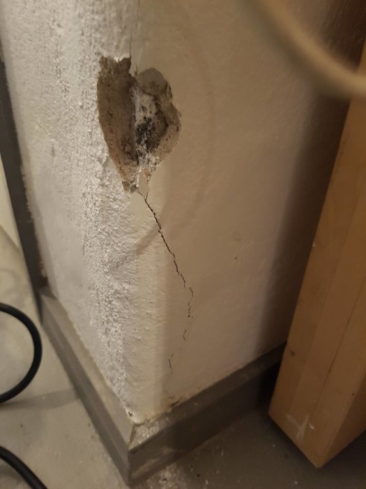 Spricka i puts på ett hörn i källare med synlig lagning och basprofil.