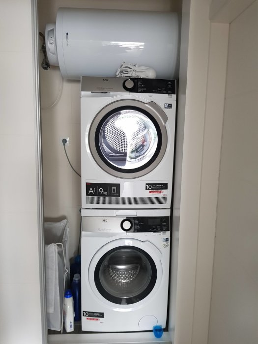 Staplad tvättmaskin och torktumlare i ett kaklat utrymme med en varmvattenberedare överst.