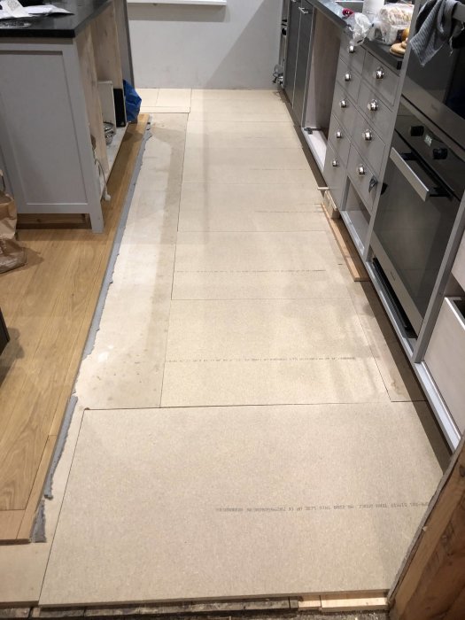 Ett halvt lagt golv med particleboard i en köksmiljö, uppbrutet golv syns vid sidan.