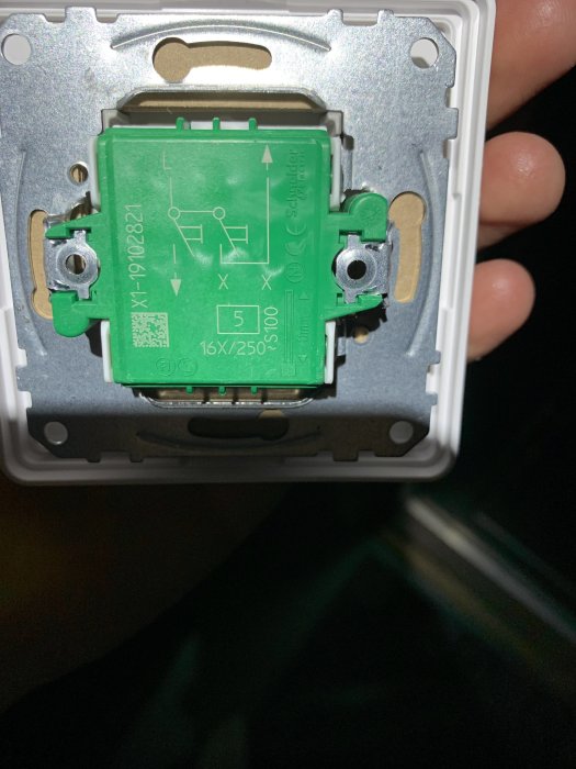 Närbild på en grön elektrisk brytare monterad i en väggdosa, synliga anslutningar och schema.