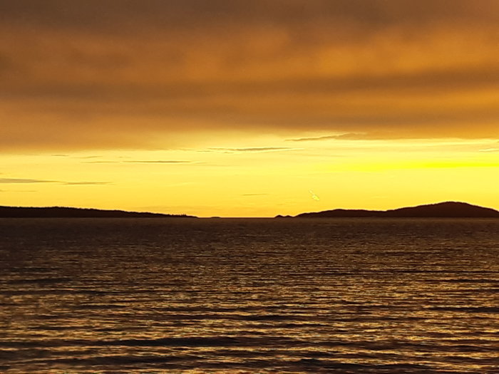 Solnedgång över havet med silhuetter av öar mot en orange himmel.