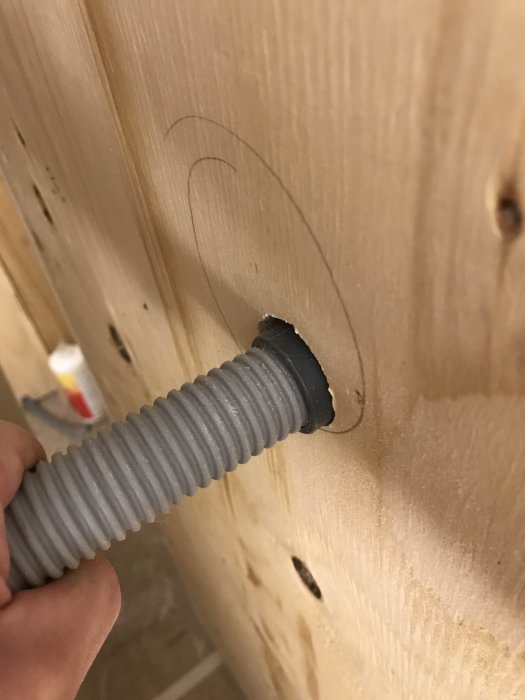Närbild på en LK rör i rör Uponor fixtur genom ett uttaget hål i en plywoodvägg, beredd för gipsning och kakling.