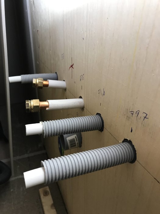VVS-installation med LK rör i rör system och fixturer på en plywoodvägg, märkt för byggprojekt.
