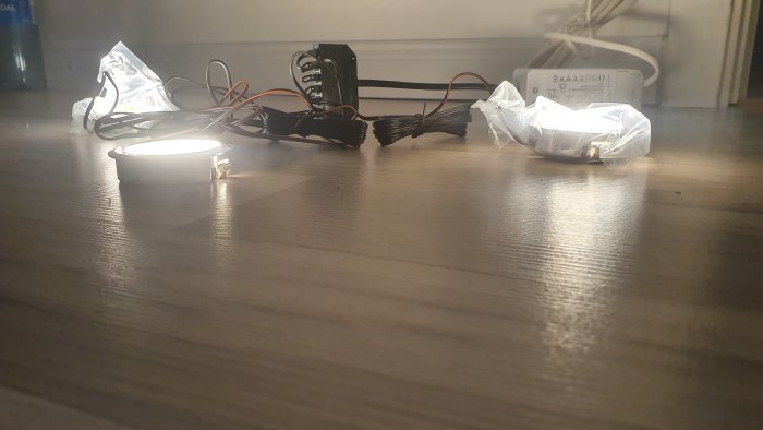 LED downlight tänd på trägolv med dimbar drivrutin och förlängningskablar intill.