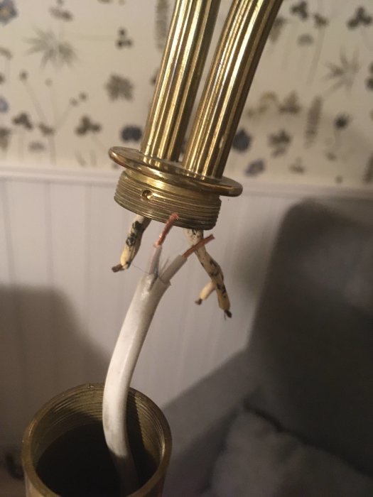 Gammal golvlampa under reparation med ny vit lampsladd, oisolerade kabeländar vid lampans metallstolpe.