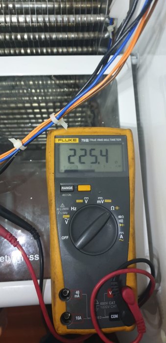 Multimeter visar 225.4 volt vid felsökning av avfrostningssystem i kylskåp.