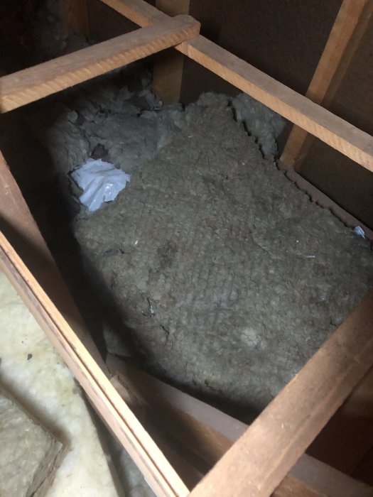 Insulation material in attic space with wooden beams, some debris visible.