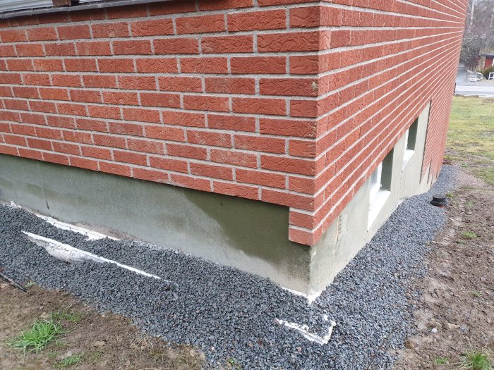 Tegelfasaden på ett suterränghus med synliga fuktfläckar vid grunden och husknuten.