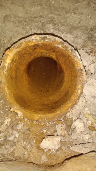 Gammal gjutjärns avloppsstam i betonggolv med synlig invändig diameter, plats för planerad wc-anslutning.