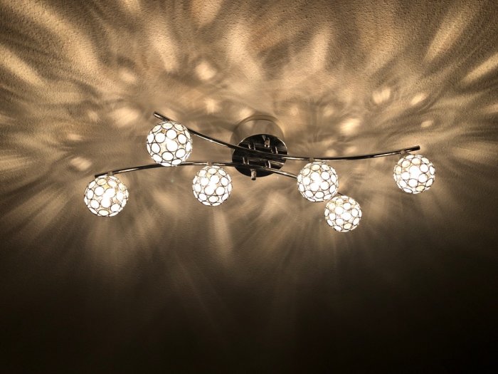Taklampa med flera ljuskällor i designade sfäriska skärmar som ger mönstrade skuggor på väggen.