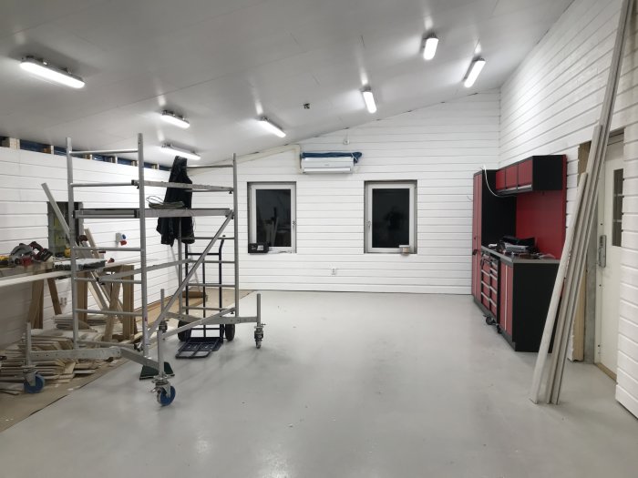 Interiör av ett ljust garage under renovering med verktyg, byggmaterial och röd förvaring.