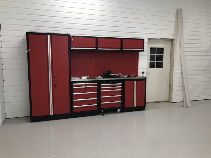 Rött och svart verktygsskåp och lådor i en ren garageinredning med synliga kablar och tillfällig elinstallation.