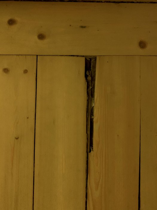 Betydande lucka mellan träplankor i ett golv, där flisor och material tydligt saknas.