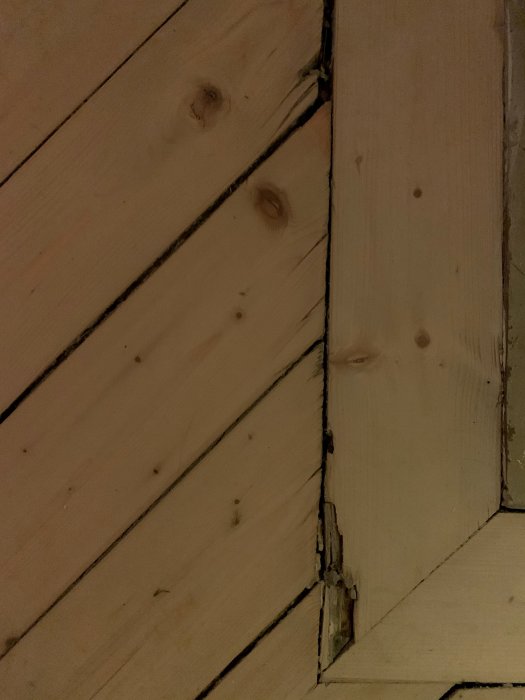 Träpanel med synliga skador och dålig passform i hörnet som tyder på slarvigt snickeriarbete.