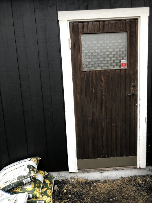 Gammal ytterdörr i garage med förberedelse för nytt nivellgolv och golvvärme, säckar med byggmaterial synliga.