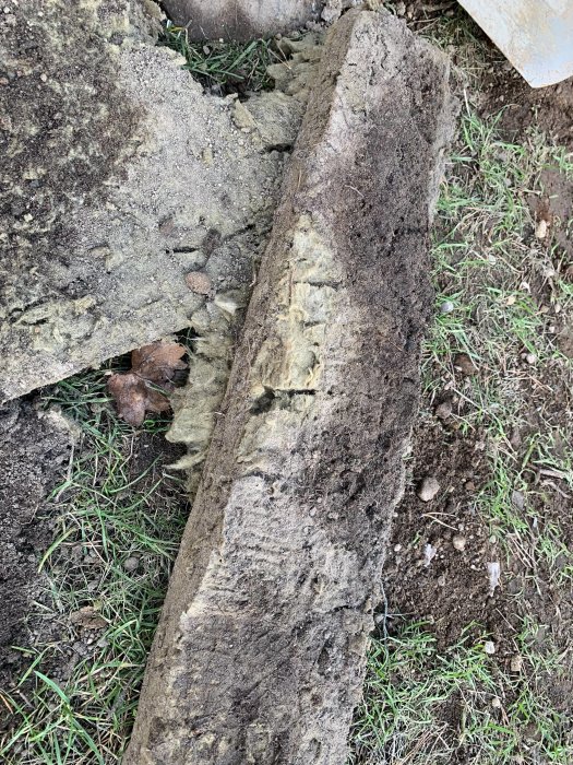 Väggisolering vid garage täckt med jord och gräs som visar vattenskador och förfall.