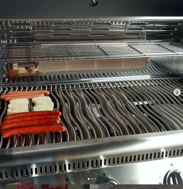 En öppen grill med korv och halloumi på grillgallret, med en sizzle-del som glöder rött.