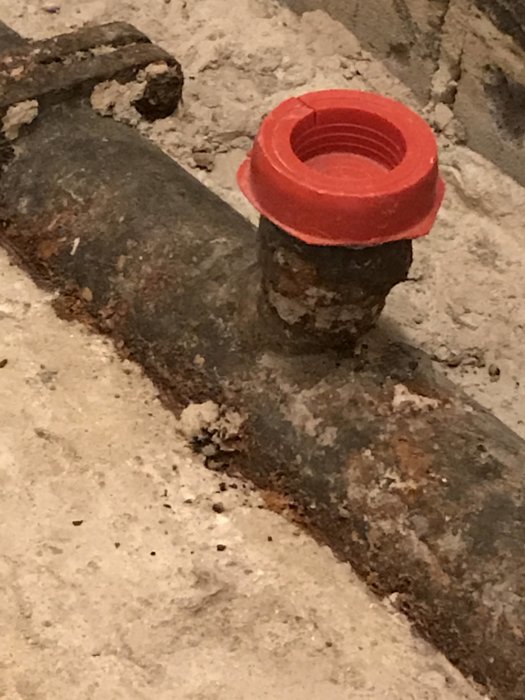 Rostfärgad röranslutning med röd plastkoppling synlig på betongunderlag.