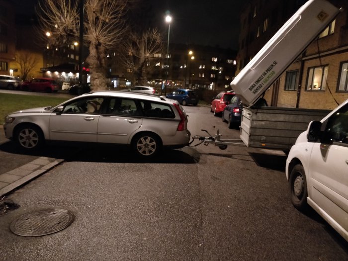 Parkerad bil bredvid en cykel med släpvagn och öppen bak på en stadsgata på kvällen.